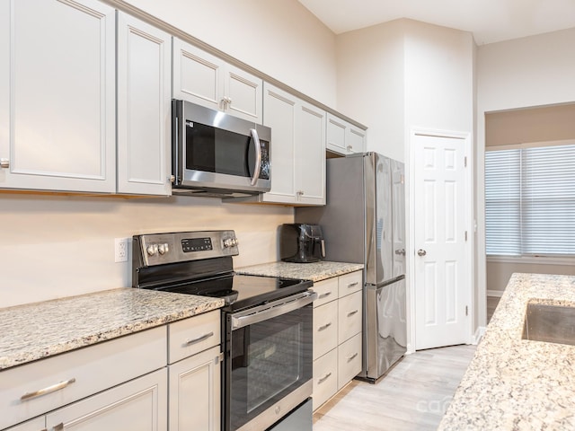 kitchen with light stone counters, light wood-type flooring, and appliances with stainless steel finishes