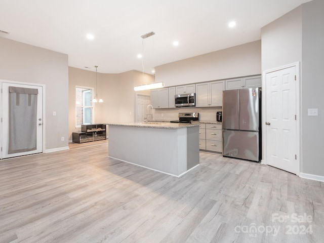 kitchen featuring light hardwood / wood-style floors, stainless steel appliances, a kitchen island with sink, decorative light fixtures, and gray cabinets