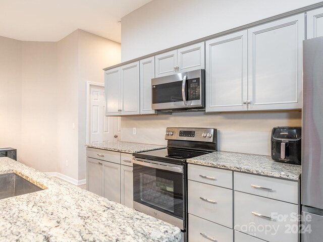 kitchen featuring light stone countertops, stainless steel appliances, gray cabinetry, and sink