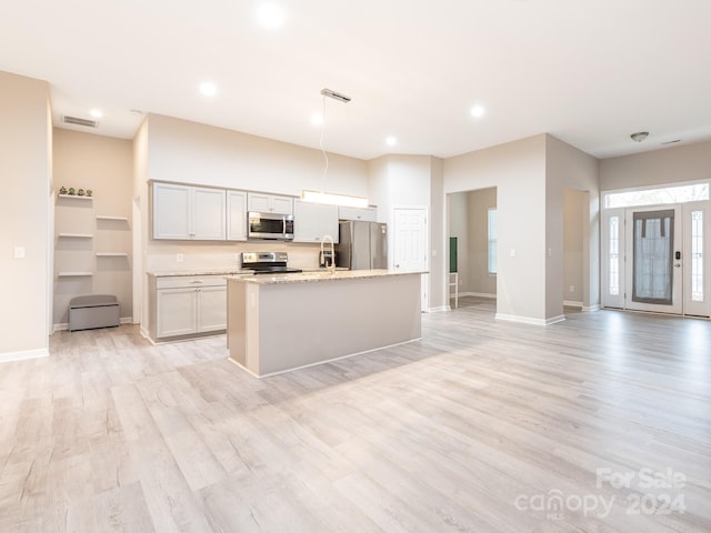 kitchen featuring light stone counters, stainless steel appliances, a kitchen island with sink, decorative light fixtures, and light hardwood / wood-style floors