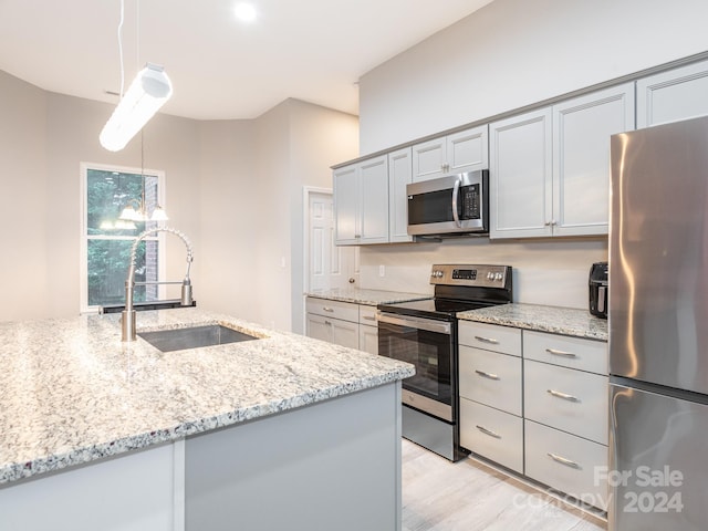 kitchen featuring light wood-type flooring, light stone counters, stainless steel appliances, sink, and pendant lighting