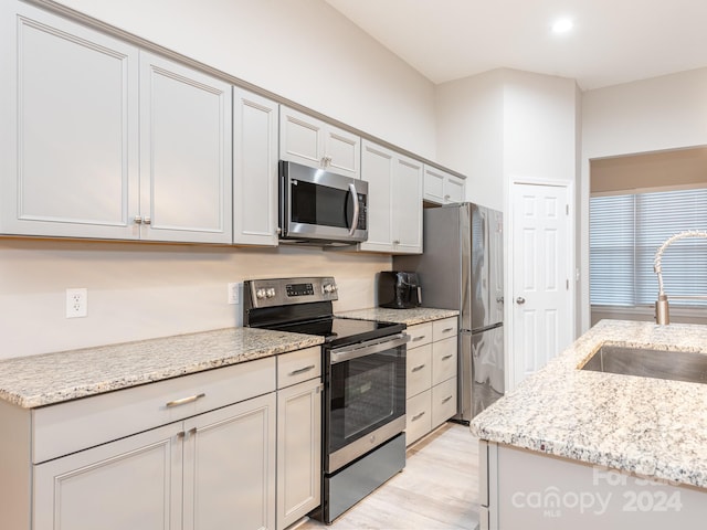 kitchen featuring light stone counters, sink, light hardwood / wood-style floors, and appliances with stainless steel finishes