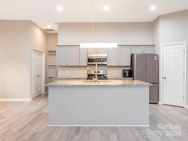 kitchen featuring light hardwood / wood-style floors, light stone countertops, a kitchen island with sink, and appliances with stainless steel finishes