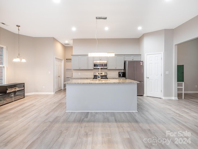 kitchen featuring light stone counters, light wood-type flooring, decorative light fixtures, and appliances with stainless steel finishes