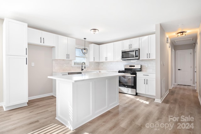 kitchen featuring appliances with stainless steel finishes, decorative light fixtures, white cabinetry, and light hardwood / wood-style floors