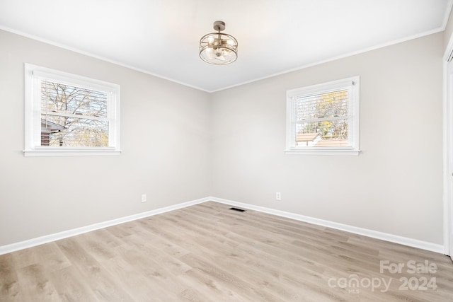 empty room featuring ornamental molding, a wealth of natural light, and light hardwood / wood-style flooring