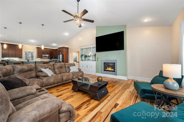 living room with ceiling fan, plenty of natural light, light wood-type flooring, and vaulted ceiling