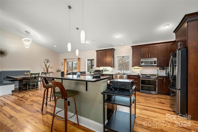 kitchen with light wood-type flooring, dark brown cabinetry, stainless steel appliances, pendant lighting, and a center island