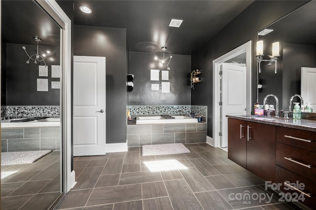 bathroom featuring tile patterned flooring, vanity, tiled tub, and an inviting chandelier