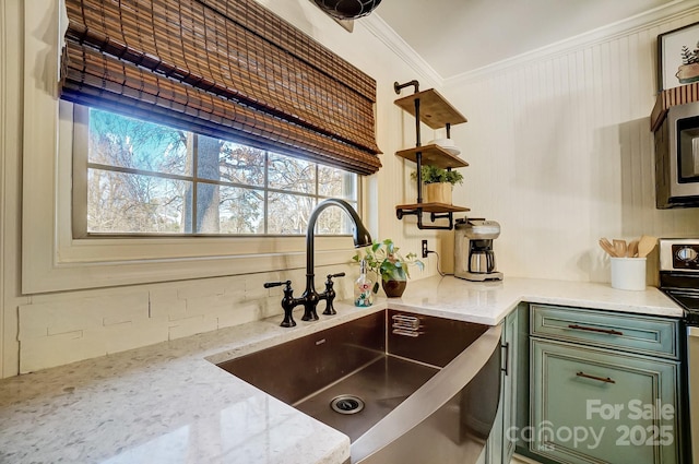 kitchen with light stone countertops, ornamental molding, sink, green cabinetry, and range