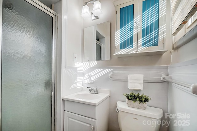 bathroom with a healthy amount of sunlight, vanity, a shower with shower door, and toilet