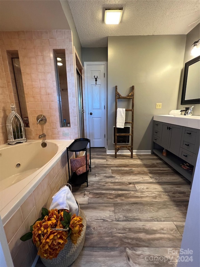 bathroom with tiled tub, vanity, wood-type flooring, and a textured ceiling