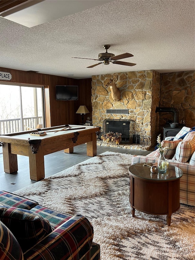 game room with ceiling fan, pool table, a stone fireplace, a textured ceiling, and hardwood / wood-style flooring