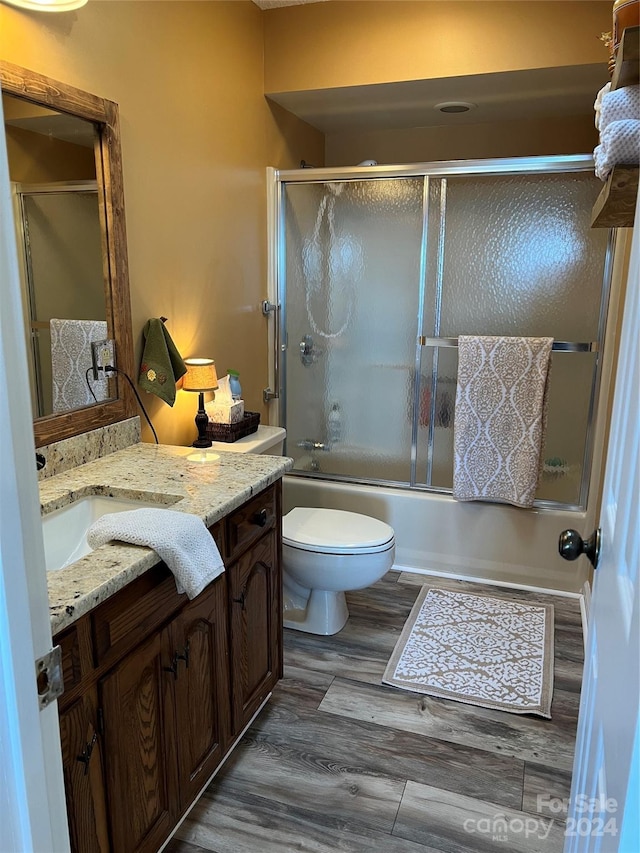 full bathroom with hardwood / wood-style floors, vanity, toilet, and shower / bath combination with glass door