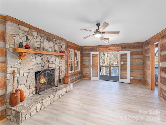 unfurnished living room featuring wood walls, a stone fireplace, french doors, and light hardwood / wood-style flooring