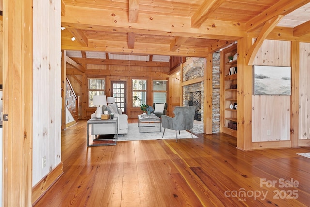 unfurnished living room with a fireplace, wood-type flooring, wooden ceiling, wooden walls, and beam ceiling