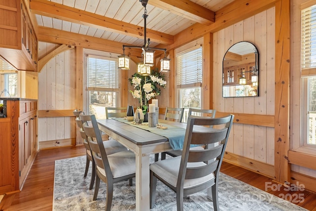 dining room with beamed ceiling, light wood-type flooring, and wood walls