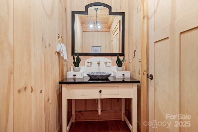 bathroom featuring vanity, a notable chandelier, hardwood / wood-style flooring, and wooden walls