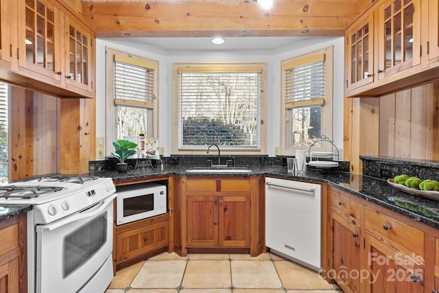 kitchen with white appliances, light tile patterned floors, sink, and dark stone countertops