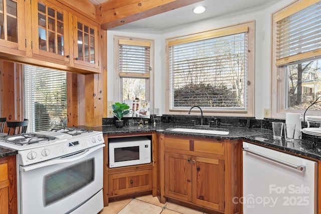 kitchen featuring light tile patterned flooring, sink, white appliances, and dark stone counters