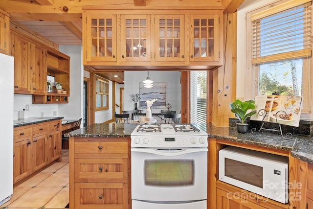 kitchen featuring dark stone countertops, a healthy amount of sunlight, pendant lighting, and white appliances