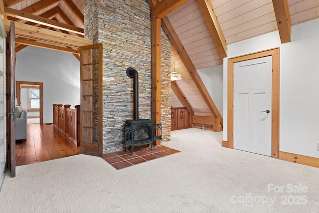 unfurnished living room with beamed ceiling, dark colored carpet, a wood stove, and high vaulted ceiling