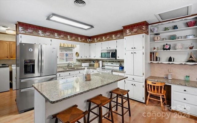 kitchen featuring washer and clothes dryer, a center island, sink, light wood-type flooring, and stainless steel appliances