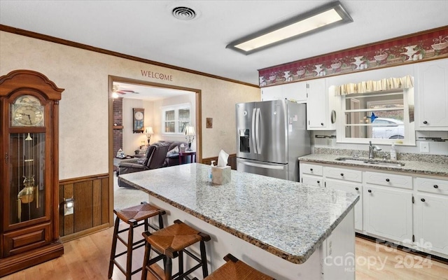 kitchen with sink, light stone counters, stainless steel fridge, white cabinets, and light wood-type flooring