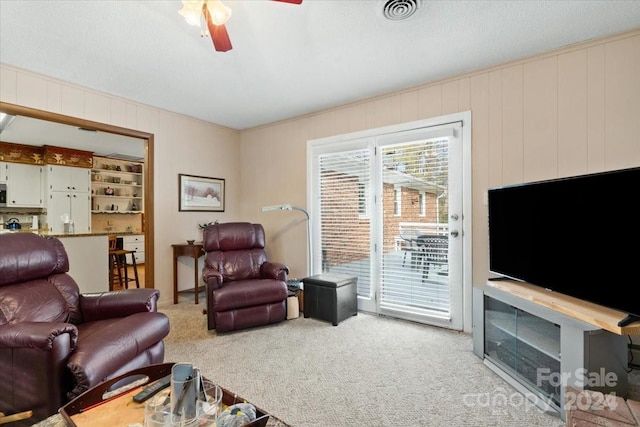 living room with a textured ceiling, light carpet, ceiling fan, and wood walls