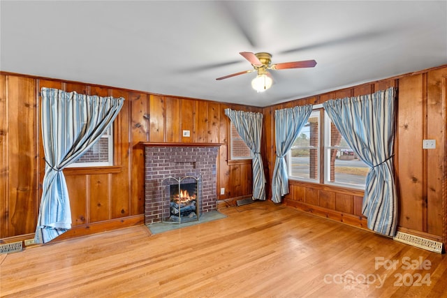 unfurnished living room with a fireplace, light hardwood / wood-style floors, ceiling fan, and wooden walls