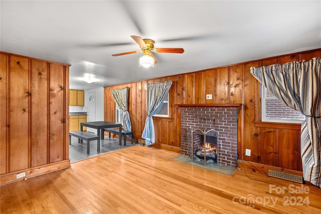 unfurnished living room featuring wooden walls, ceiling fan, light hardwood / wood-style floors, and a brick fireplace