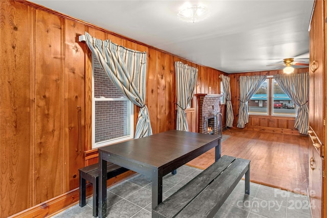 dining room featuring ceiling fan, a fireplace, tile patterned flooring, and wooden walls