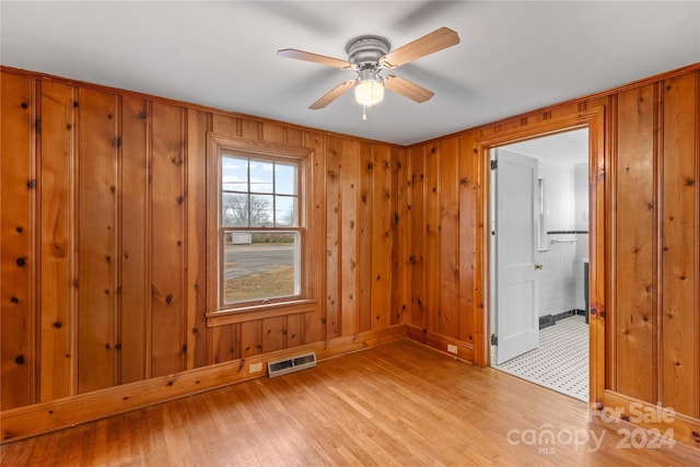 empty room with light hardwood / wood-style floors, ceiling fan, and wood walls