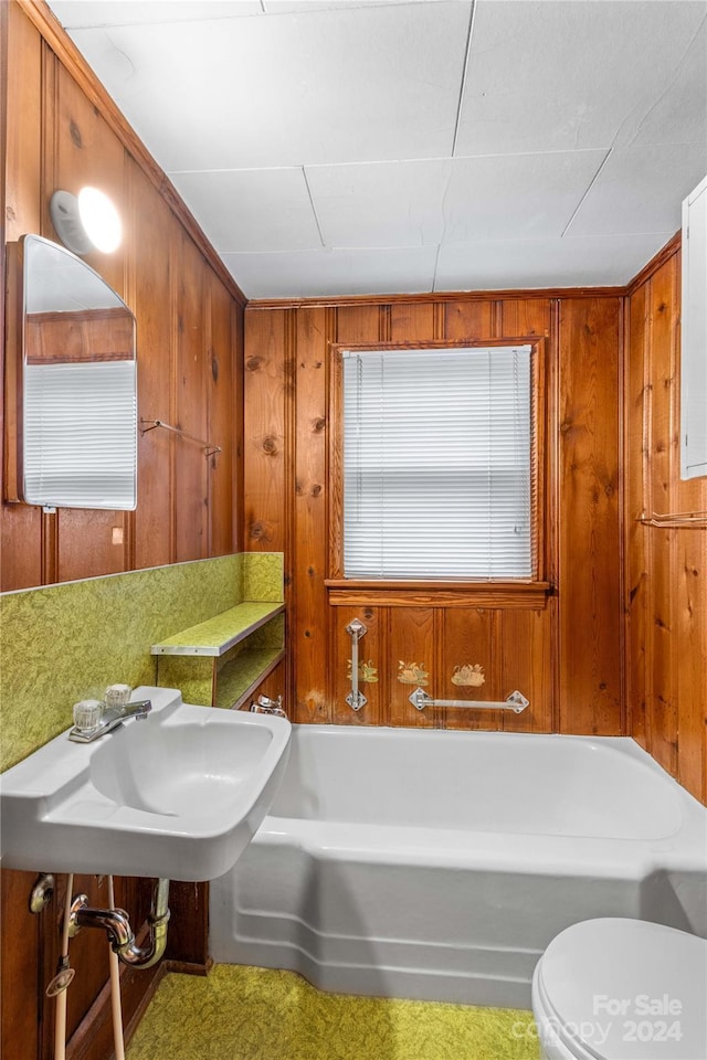 bathroom with a bath, toilet, wooden walls, and sink