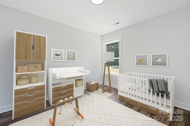 bedroom with a nursery area, visible vents, light wood-style flooring, and baseboards