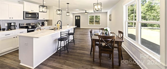 kitchen with stainless steel appliances, light countertops, hanging light fixtures, a kitchen island with sink, and white cabinetry