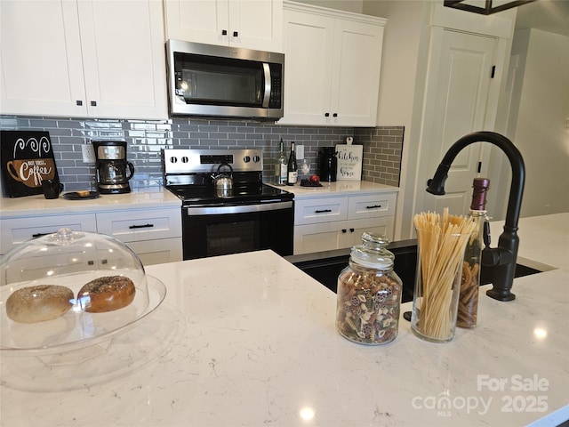 kitchen featuring stainless steel appliances, light stone counters, white cabinetry, and tasteful backsplash