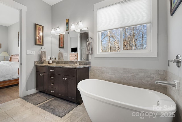 ensuite bathroom featuring double vanity, ensuite bath, tile patterned flooring, a freestanding tub, and a sink