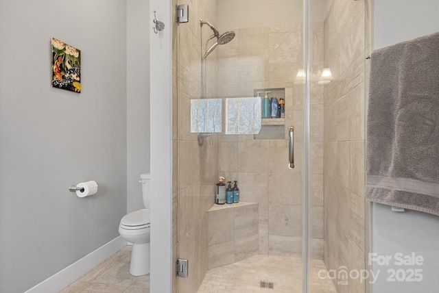 full bath with toilet, a stall shower, and baseboards