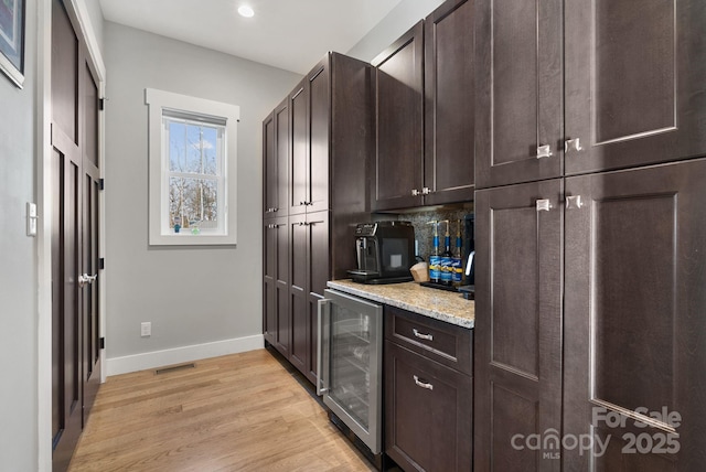 kitchen featuring wine cooler, visible vents, baseboards, dark brown cabinets, and light wood-type flooring