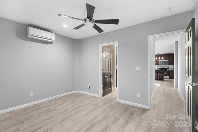 unfurnished bedroom featuring light wood-style floors, an AC wall unit, ceiling fan, and baseboards