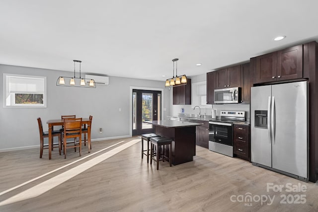 kitchen with a wall unit AC, dark brown cabinetry, a kitchen island, appliances with stainless steel finishes, and light wood-type flooring