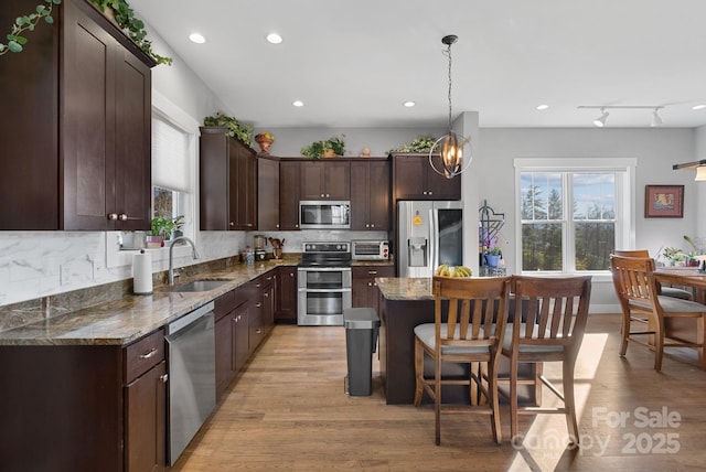 kitchen with dark brown cabinetry, appliances with stainless steel finishes, a center island, a sink, and a wealth of natural light