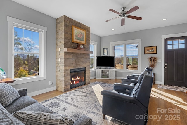 living room featuring recessed lighting, ceiling fan, a stone fireplace, wood finished floors, and baseboards