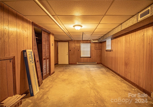 basement with baseboard heating, wooden walls, and a drop ceiling