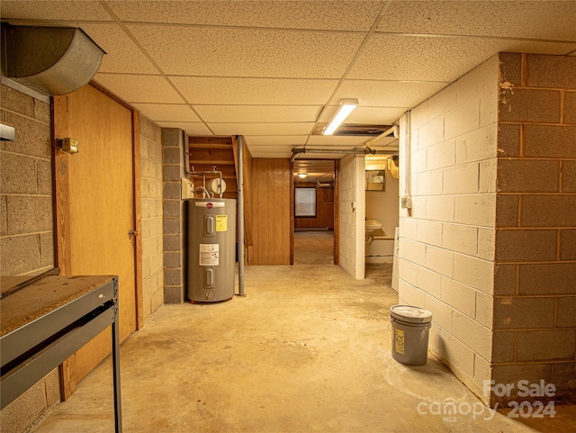 basement with a paneled ceiling, water heater, and wooden walls