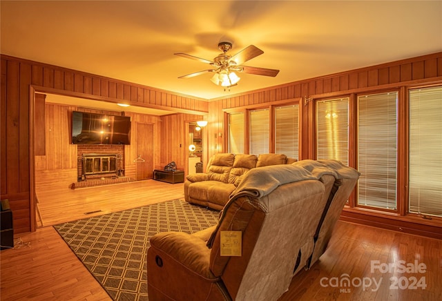 living room featuring a fireplace, wood-type flooring, ceiling fan, and wooden walls