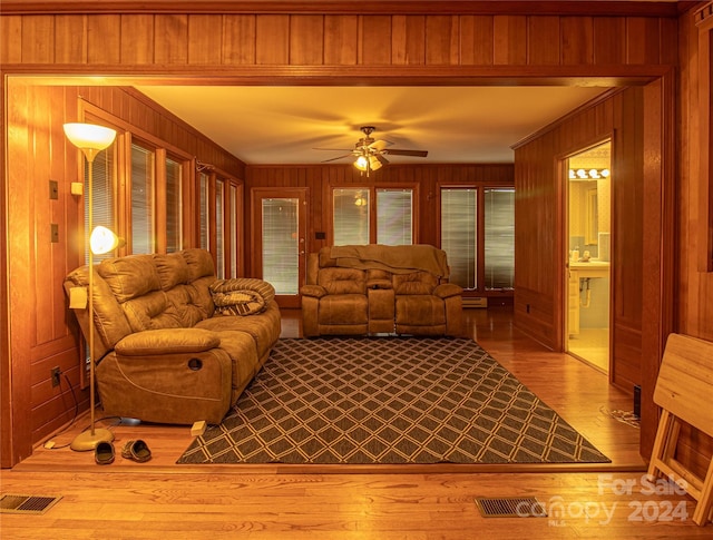 living room with ceiling fan, wooden walls, and light hardwood / wood-style flooring