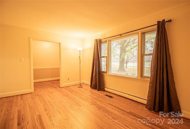 unfurnished room featuring light hardwood / wood-style floors, crown molding, and a baseboard heating unit