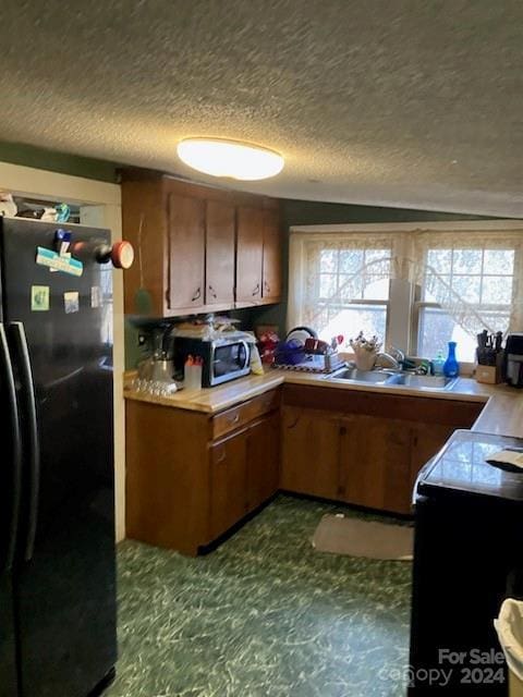 kitchen featuring a textured ceiling, black fridge, and sink